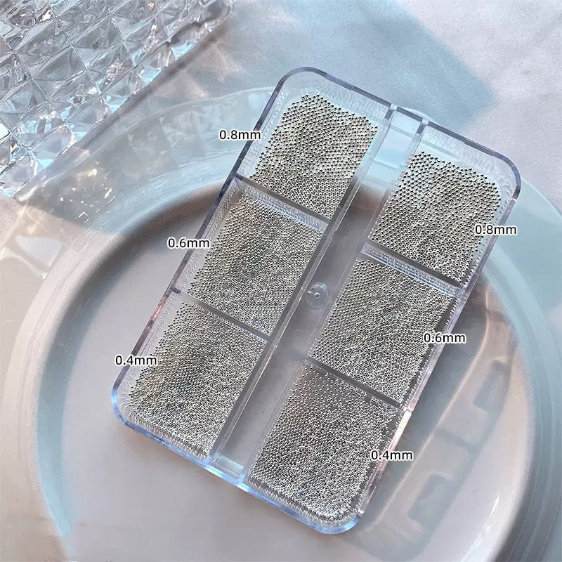 Silver steel nail art beads in six compartments labeled 0.4 to 0.8 mm