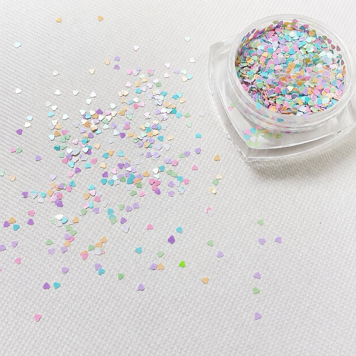 Pastel multicolor mini heart nail glitter scattered beside a clear jar