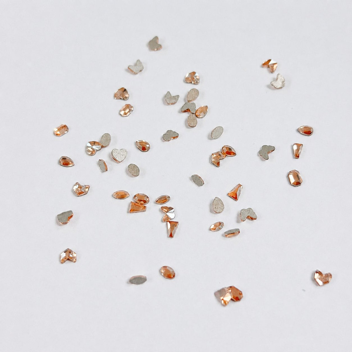 Mixed-size champagne rhinestone embellishments scattered on a white surface