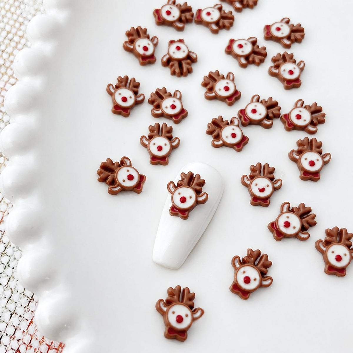 Brown reindeer nail charms with red and white details on a sample nail tip
