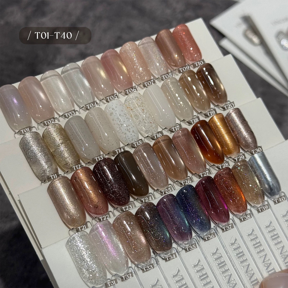 A nail color swatch display card showing multiple false nail tips in various finishes and shades, including matte, glossy, glitter, and metallic tones. The top-left corner has a label reading '/ TO1-T40 /', and the card shows the brand name YEHANAI vertically along the bottom edge.