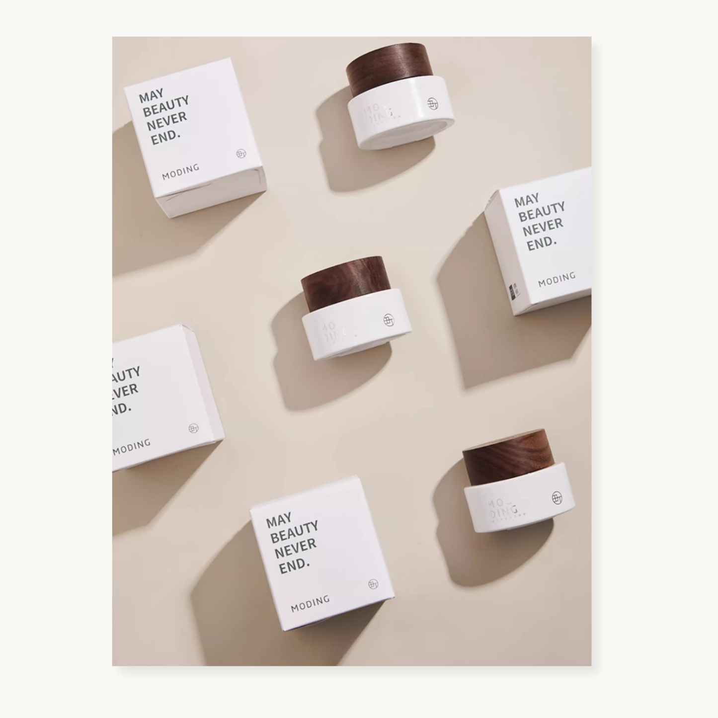 Flat lay display of MODING skincare cream jars and boxes on a beige background. White packaging with the phrase ‘MAY BEAUTY NEVER END.’ and wooden-texture lids, arranged neatly in soft natural light.