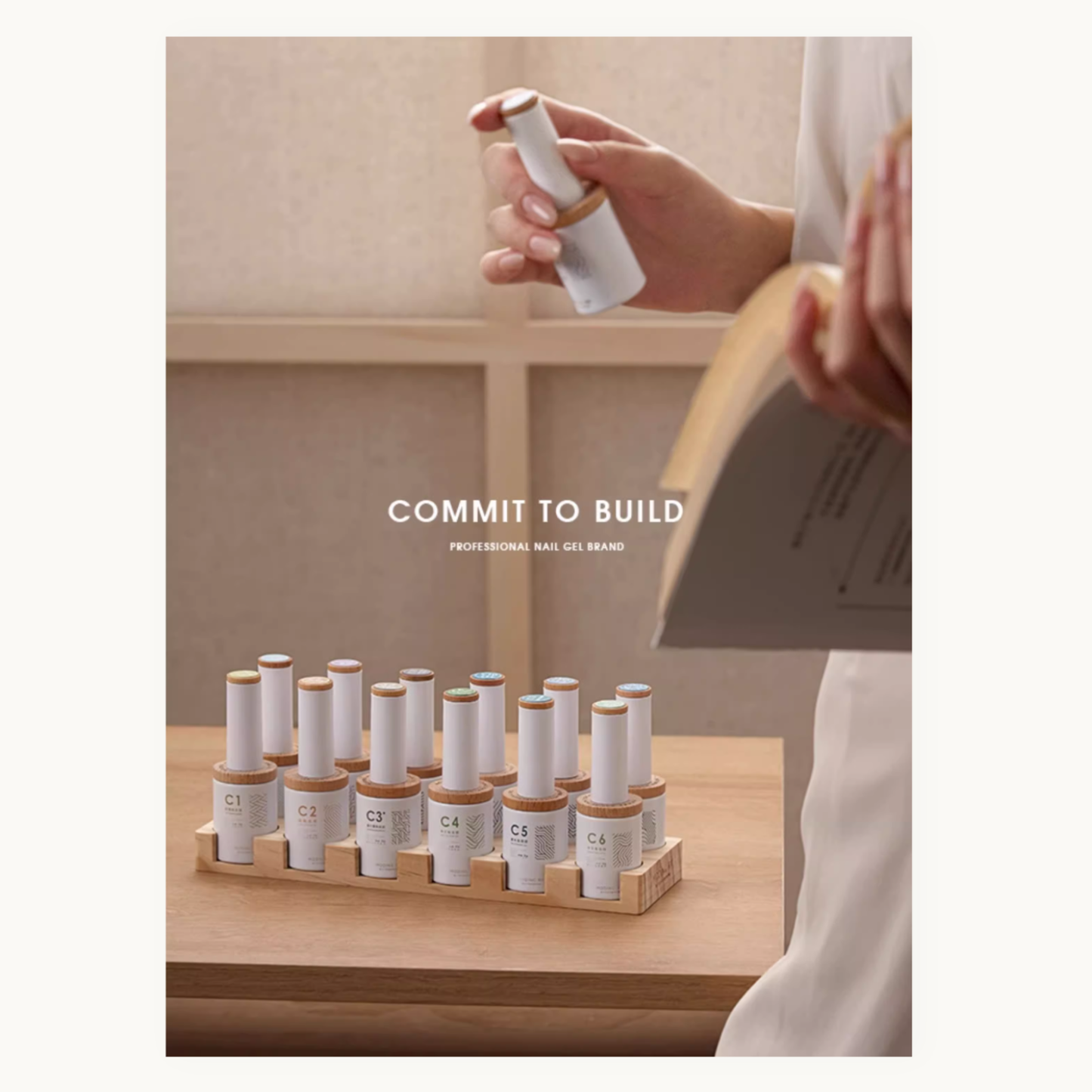 Hand holding a moding gel bottle over a wooden stand with multiple cylindrical containers on a light-colored surface.