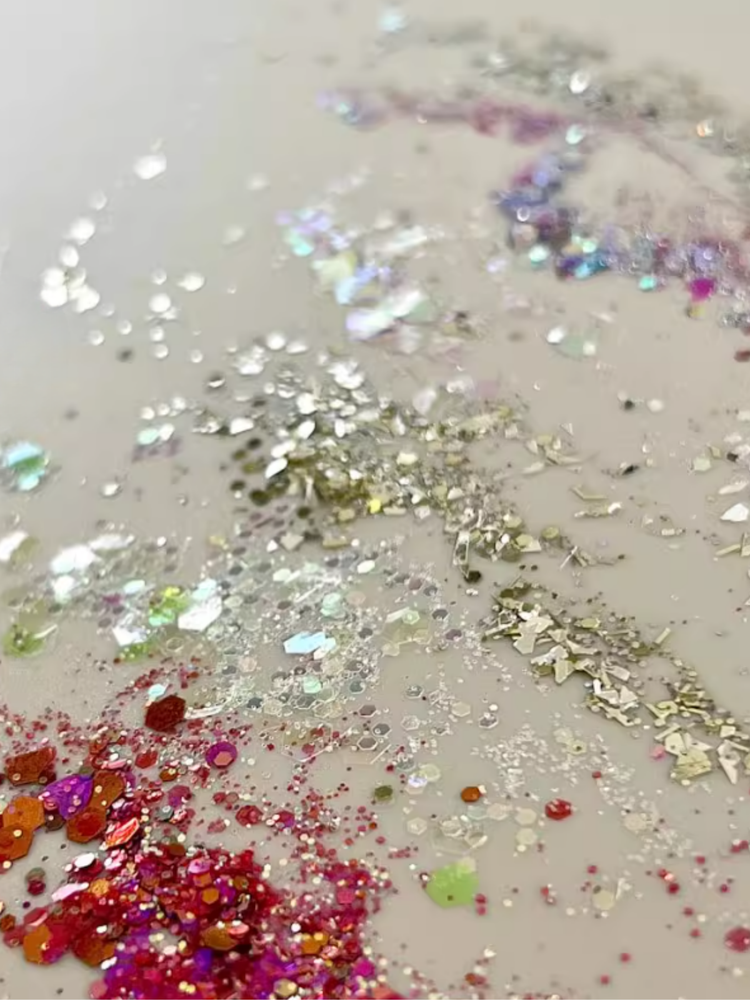 A soft minimalist photo showing iridescent nail glitters, opal flakes, and shimmer dusts arranged elegantly in small jars, reflecting light with delicate pastel tones.