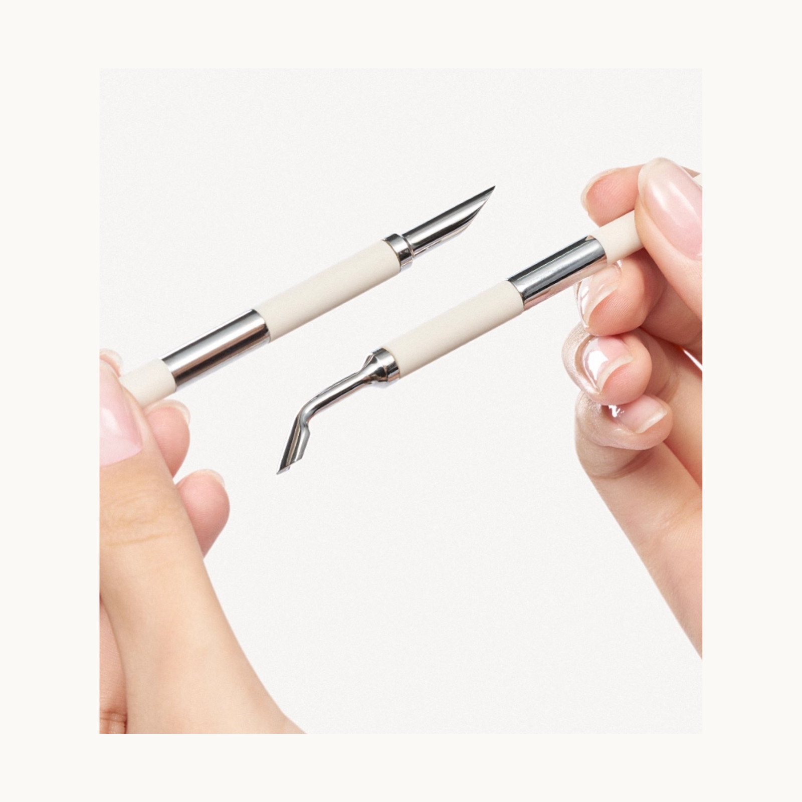 Close-up of hands holding dual-ended stainless steel nail art tools, showing the angled and pointed tips.