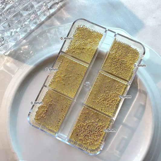 Gold steel nail art beads in six compartments labeled 0.4 to 0.8 mm