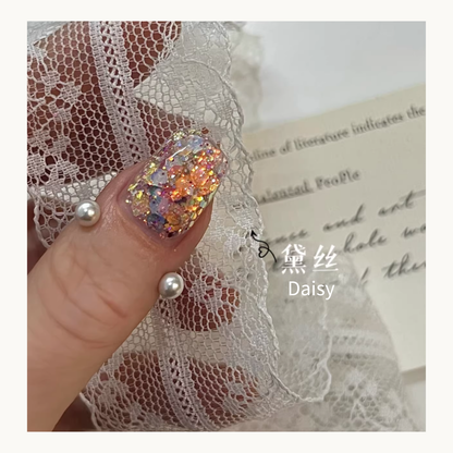 Close-up of Daisy glitter applied on a nail featuring warm orange and iridescent hexagonal sequins against white lace.