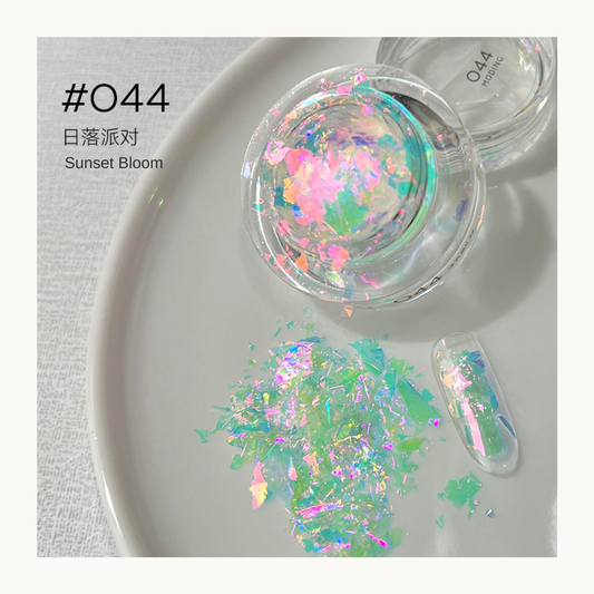 Pink, aqua, and green iridescent nail art flakes in a jar with a decorated swatch