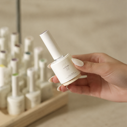MR NAIL White gel polish bottle held in hand against a softly blurred nail salon background.