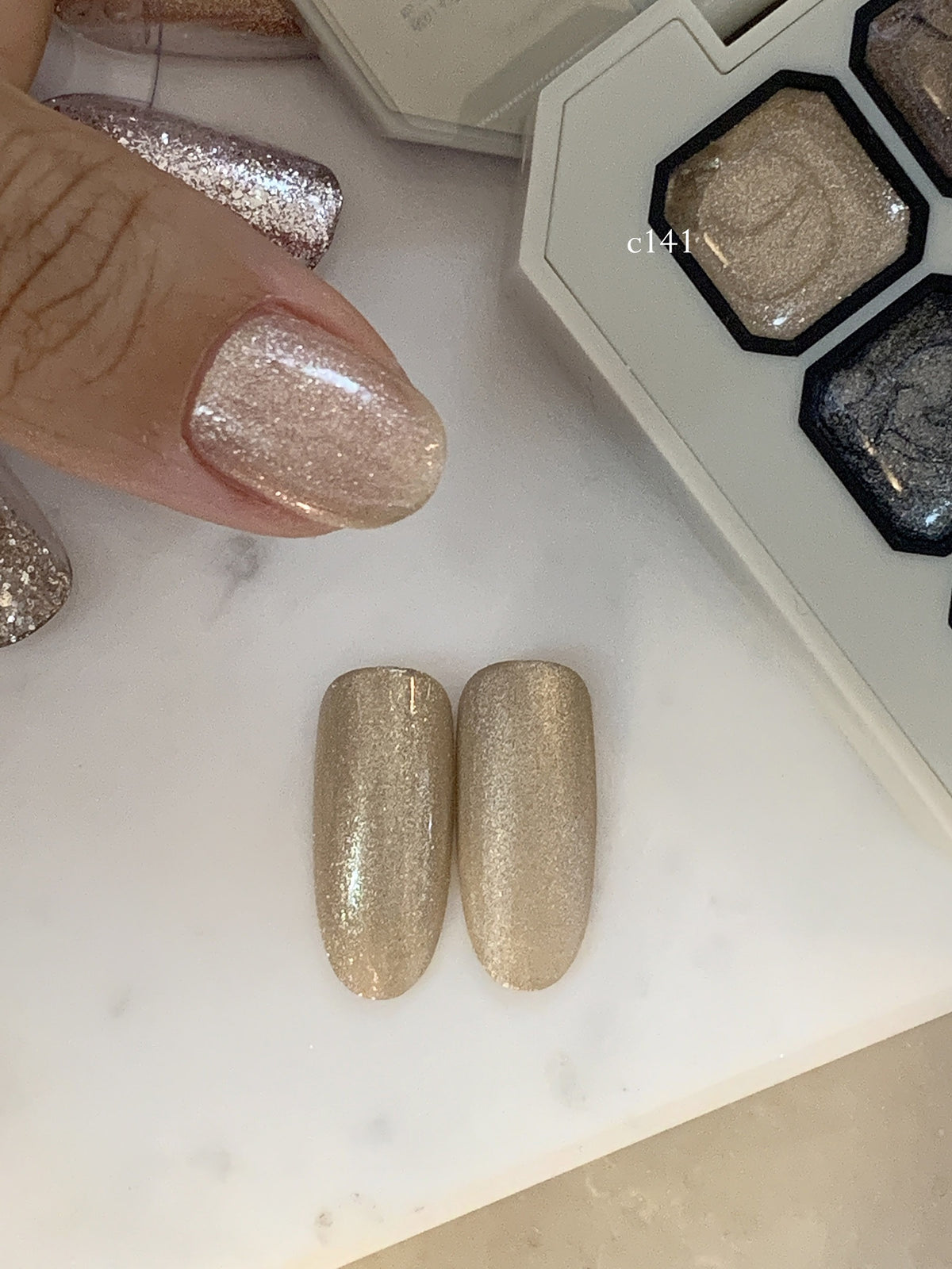 Close-up of champagne-pink shimmer gel on a fingernail beside the palette