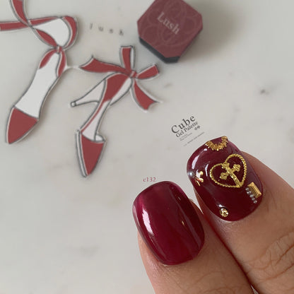 Close-up of deep burgundy soft gel manicure with gold charms
