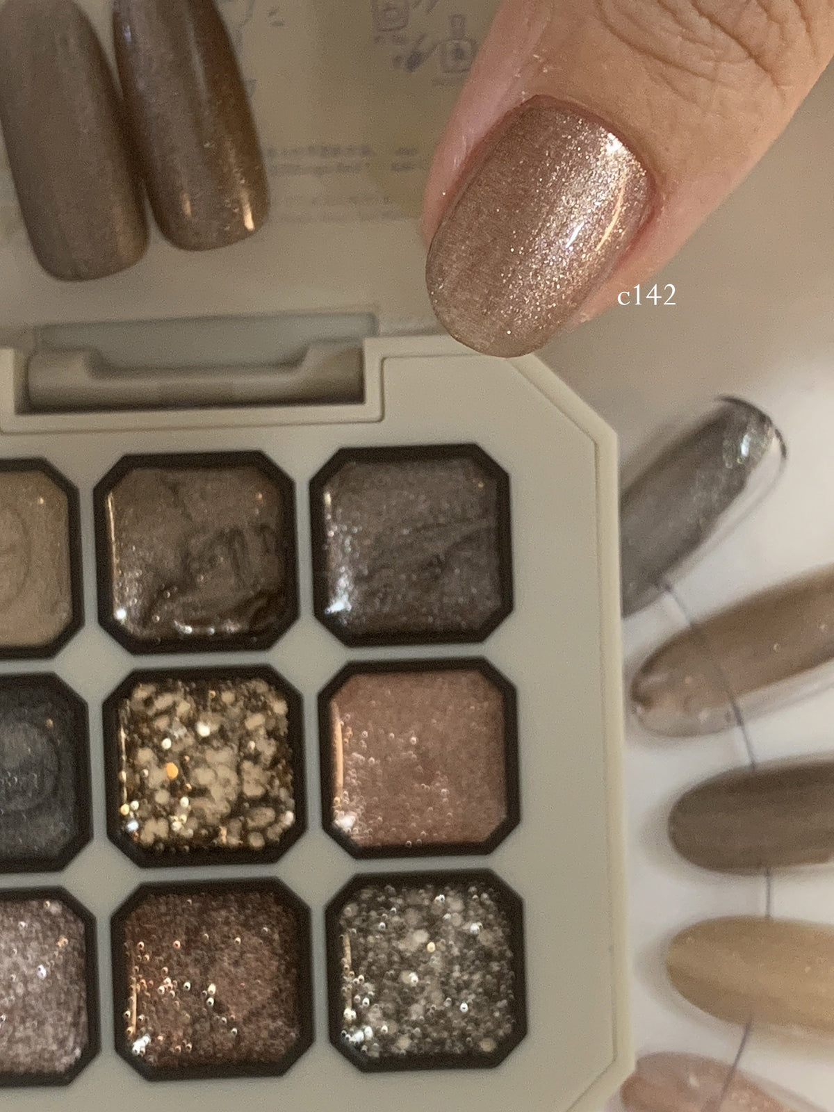 Close-up of rose-gold glitter gel on a fingernail beside the palette